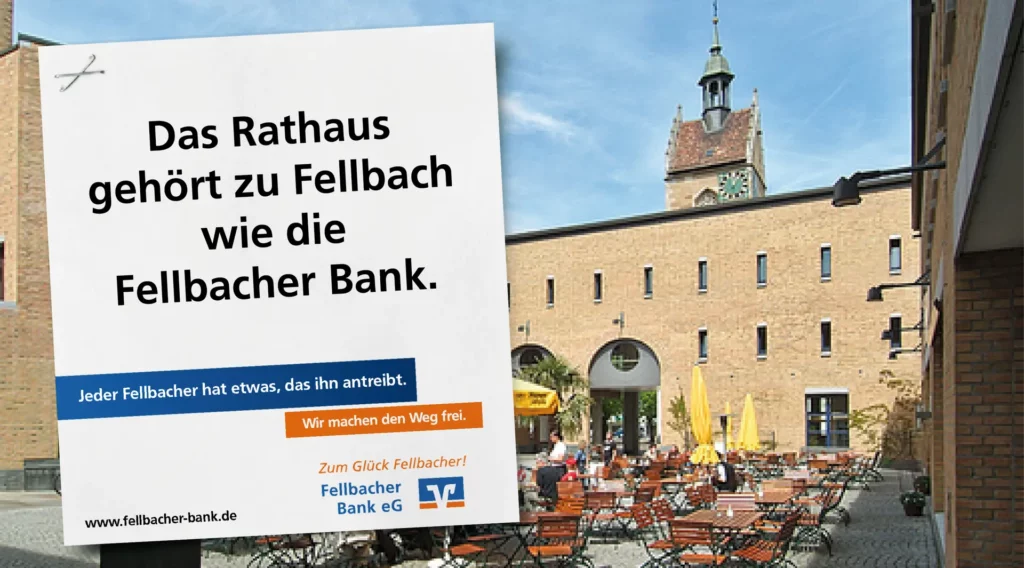 Großflächenmotiv der Fellbacher Bank mit dem Claim ‚Das Rathaus gehört zu Fellbach wie die Fellbacher Bank‘, aufgenommen auf dem Rathausplatz mit Außengastronomie und dem historischen Uhrturm.