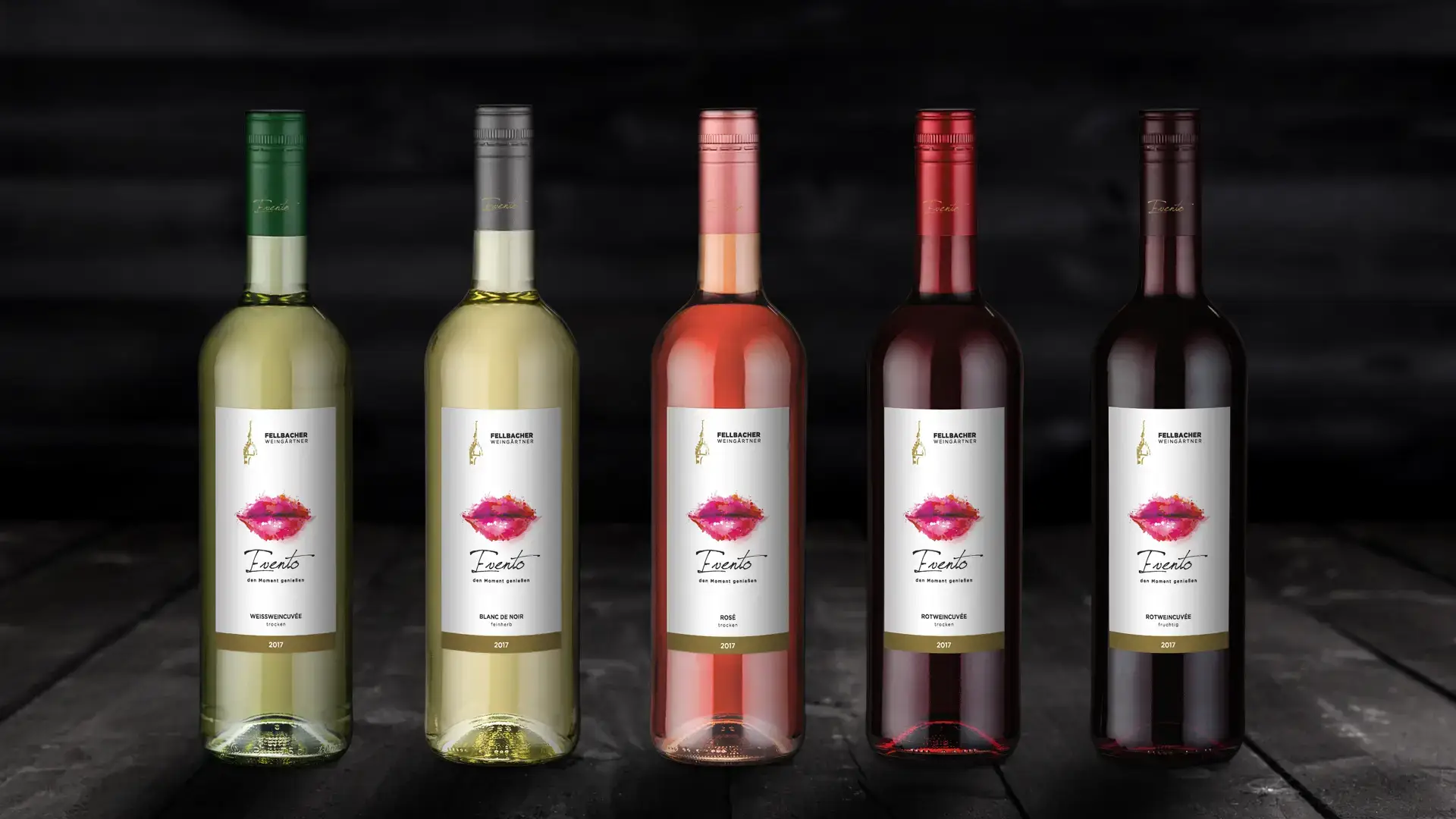 Fünf Flaschen Wein der Marke Fellbacher, darunter Weißwein, Rosé und Rotwein, präsentiert vor einem dunklen Hintergrund. Die Etiketten zeigen das Wort "Evento" und ein Lippenmotiv, das die Qualität und den Genuss der Weine symbolisiert.