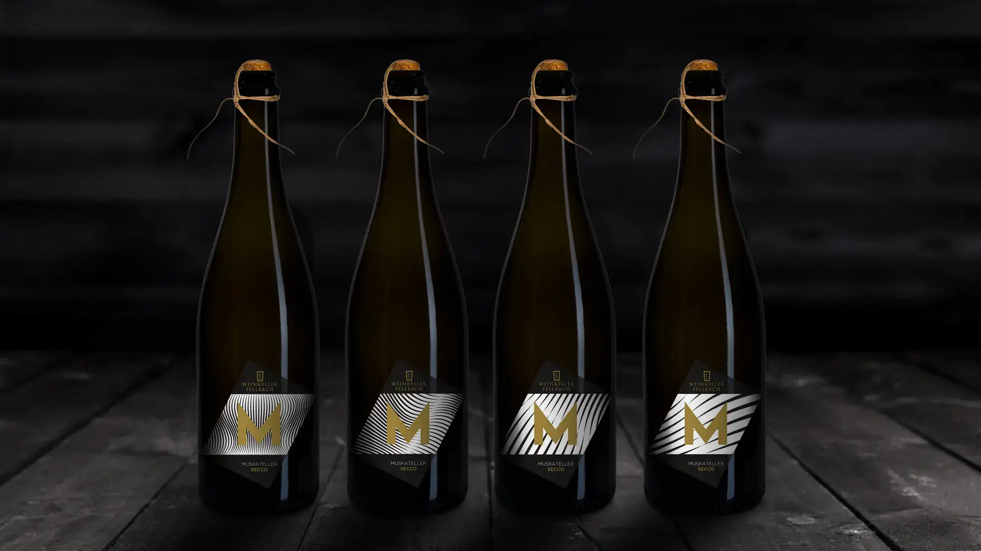Vier Flaschen Muskateller Secco auf einem dunklen Holztisch, jede mit einem einzigartigen Etikettendesign, das das elegante Branding der Weinkellerei zeigt.
